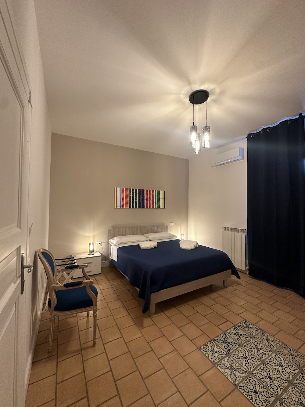 Camera matrimoniale: letto con copriletto blu e pavimento in cotto